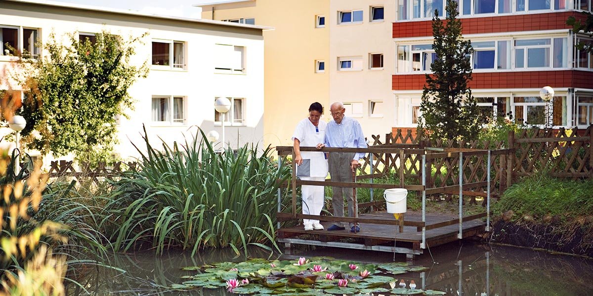 Eine Mitarbeiterin und ein älterer Mann neben Teich
